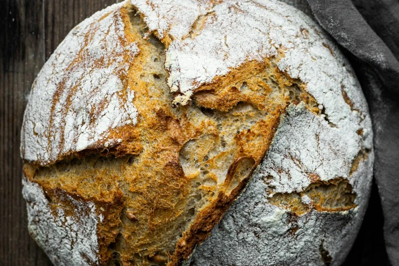 Rustic country sourdough bread loaf with scored flour crust on wooden table